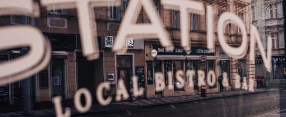 Skiltet «Local Bistro» speiles i et butikkvindu mot en bygate