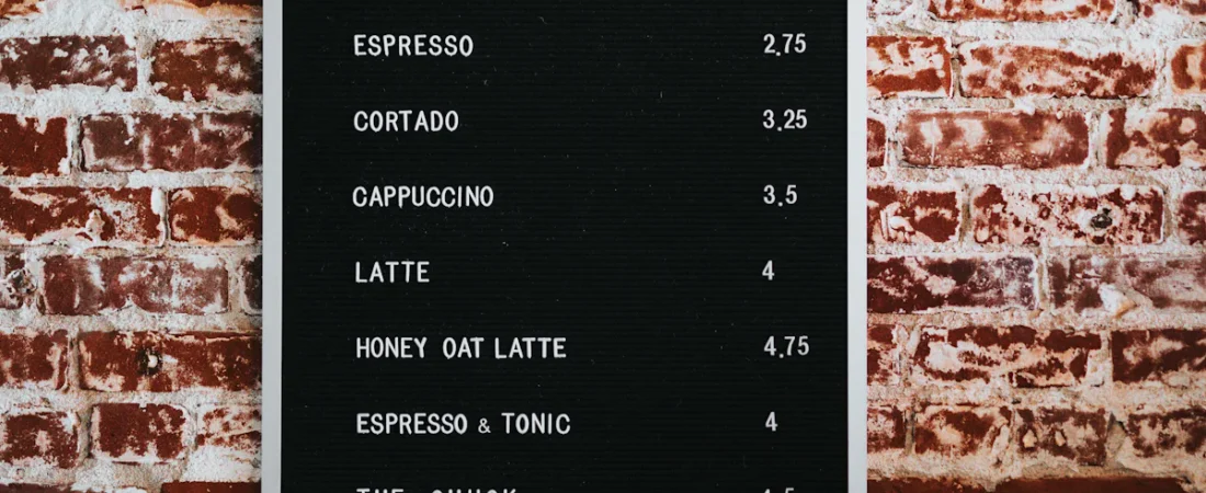 En enkel menytavle med kaffeutvalg og priser på en murvegg