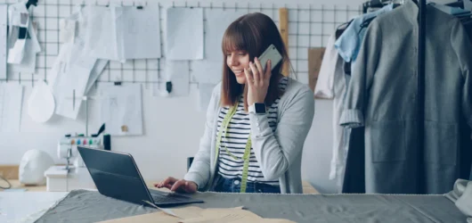 Eier av en liten bedrift arbeider på laptop mens hun snakker i telefonen